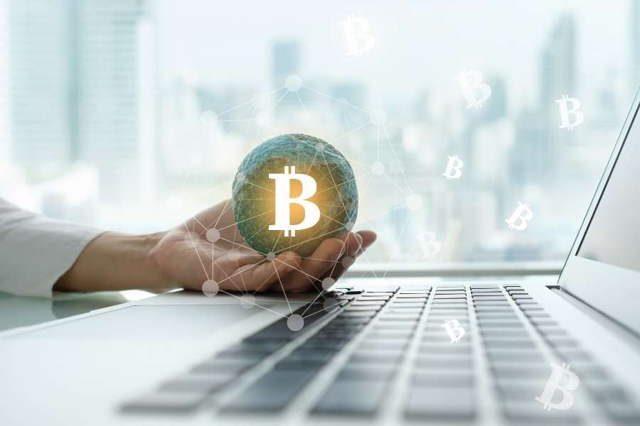 Une main tient un globe terrestre avec le logo Bitcoin stylisé, au-dessus d'un ordinateur portable, symbolisant un projet crypto mondial.