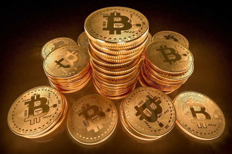 Plusieurs piles de pièces dorées de Bitcoin disposées sur une surface sombre pour illustrer la constitution d'un portefeuille crypto.