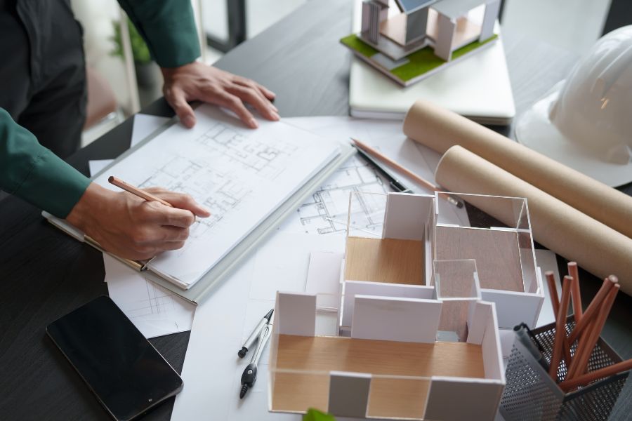 Un architecte dessine des plans sur un carnet entouré de maquettes de maisons pour la conception architecturale.